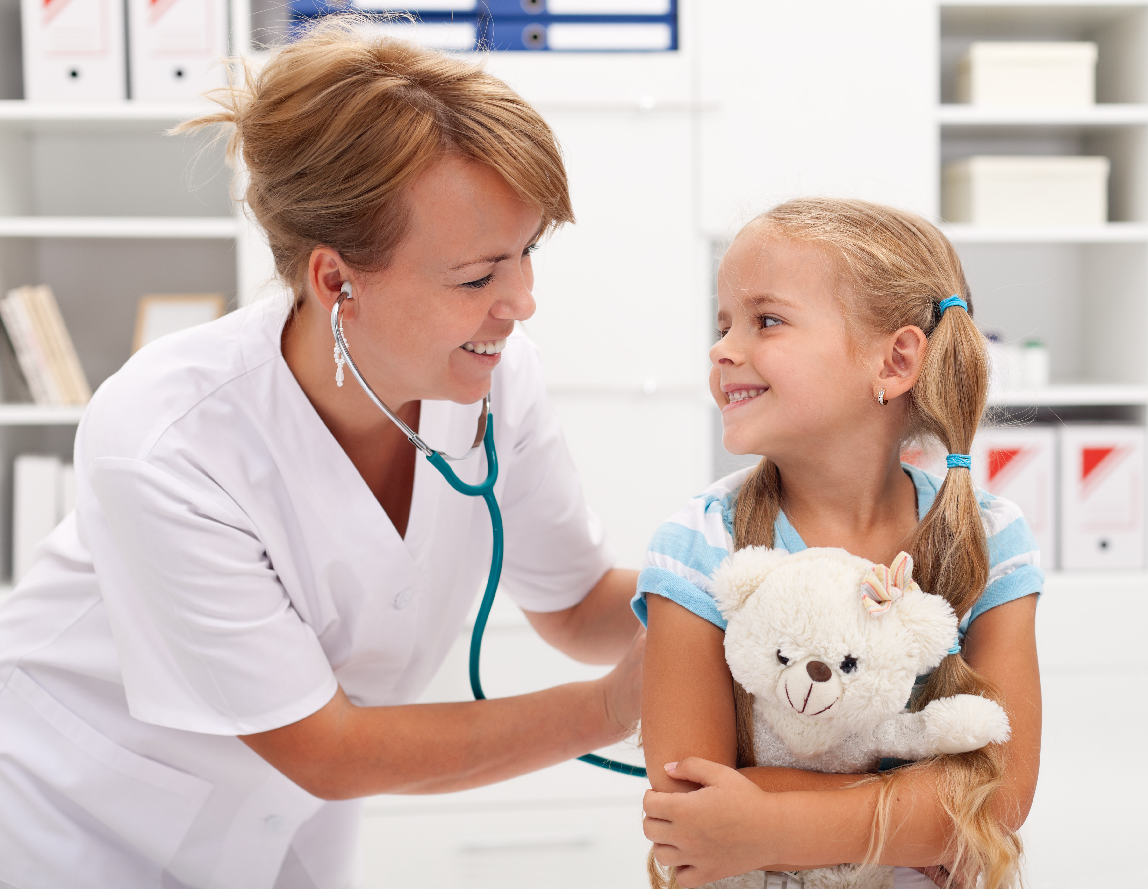 Happy little girl at the doctor for a checkup - being examined with a stethoscope