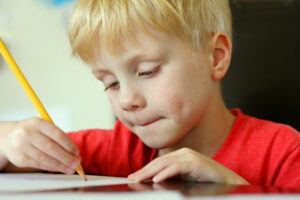 a young, preschool aged child is drawing on a white piece of paper with a writing pencil