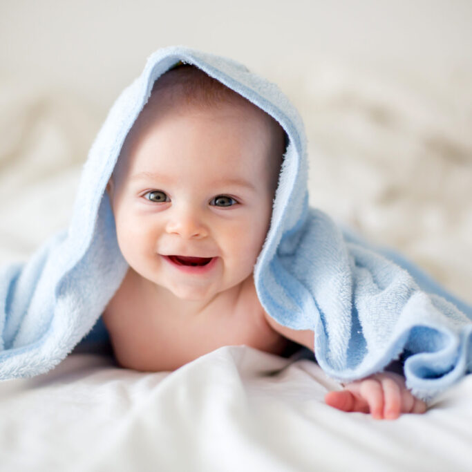 Cute little baby boy, relaxing in bed after bath, smiling happily, daytime