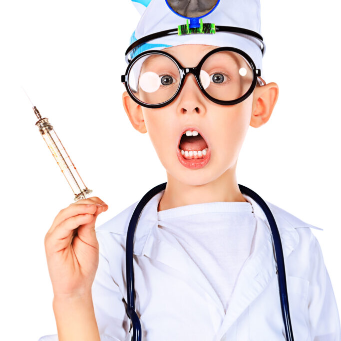 Portrait of a funny boy in big spectacles playing doctor with syringe and a stethoscope. Isolated over white.
