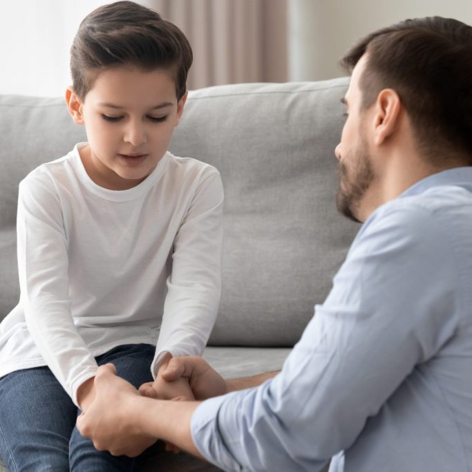 Worried single father comforting upset kid son helping with problem Worried loving young single father holding hand talking comforting upset little kid son sharing helping with problem, caring dad foster parent give support apologizing supporting listening child boy